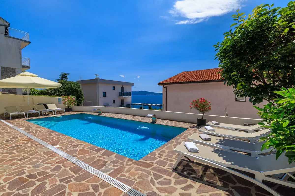 A rooftop pool with stone flooring, lounge chairs, and a view of the sea.