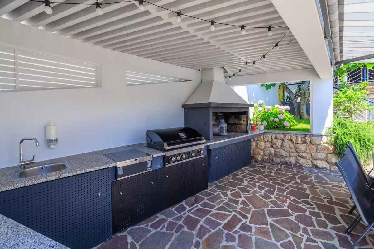An outdoor kitchen with a stone-tiled patio, a built-in sink, and a grill.