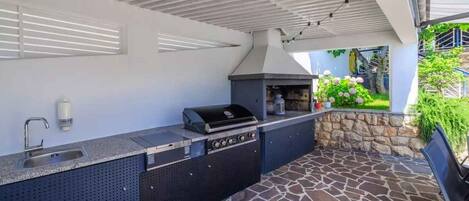 An outdoor kitchen with a stone-tiled patio, a built-in sink, and a grill.