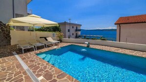Una piscina con sillones de descanso y sombrillas, un patio de piedra y vistas al mar.