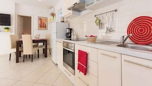A modern kitchen with white cabinets, a dining area with a table and chairs, and a red towel hanging on the oven door. - Holiday apartment 50 m from the beach (Čižići)