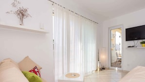 A modern living room with a sofa, a small table, and a red rug. There is a TV mounted on the wall and a door leading to another room. - Holiday apartment 50 m from the beach (Čižići)