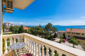 Un balcon avec une table et des chaises carrelées, donnant sur une zone côtière avec des bâtiments et des arbres.