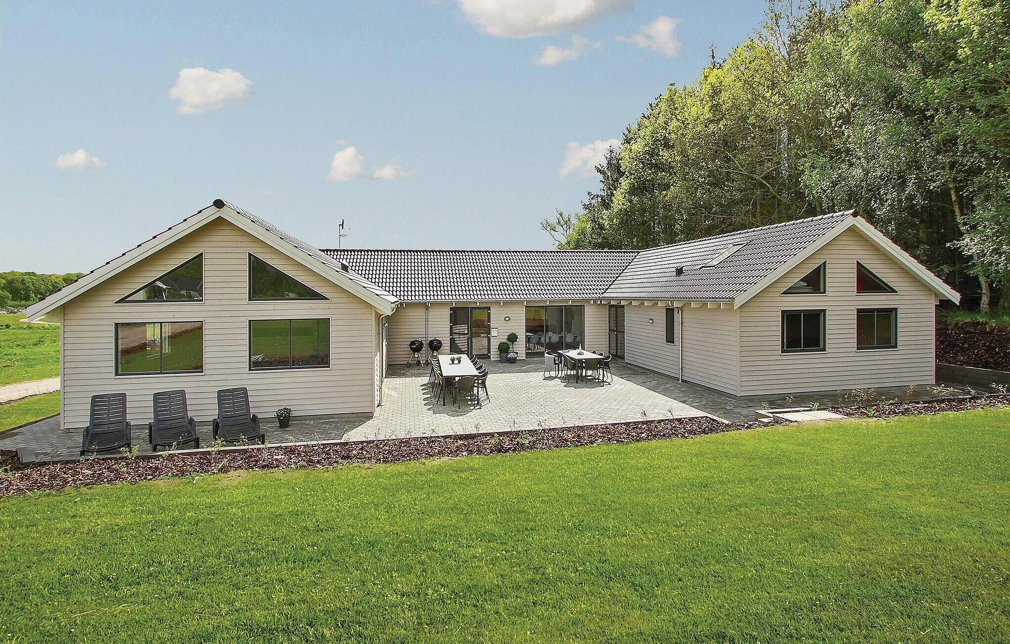 Una casa a due piani con patio, ampie finestre e un giardino.