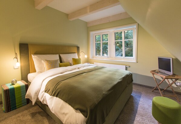 Une chambre à coucher avec un lit, une lampe de chevet, une fenêtre et un téléviseur posé sur une petite table.