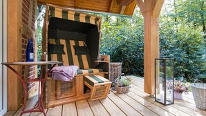 Une terrasse en bois avec un espace salon extérieur doté de coussins, une table et une structure vitrée.
