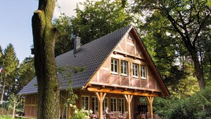 Une maison traditionnelle en bois, dotée d’un grand porche, entourée d’une végétation luxuriante et d’une pelouse bien entretenue.