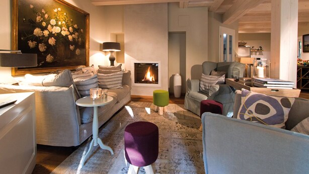 Un salon chaleureux avec une cheminée, des fauteuils confortables et un grand tableau représentant des fleurs.