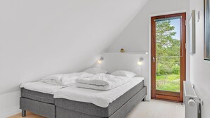 A modern bedroom with a loft bed, white bedding, and a view of greenery through a glass door. - Amazing home in Rømø with sauna (Rømø)