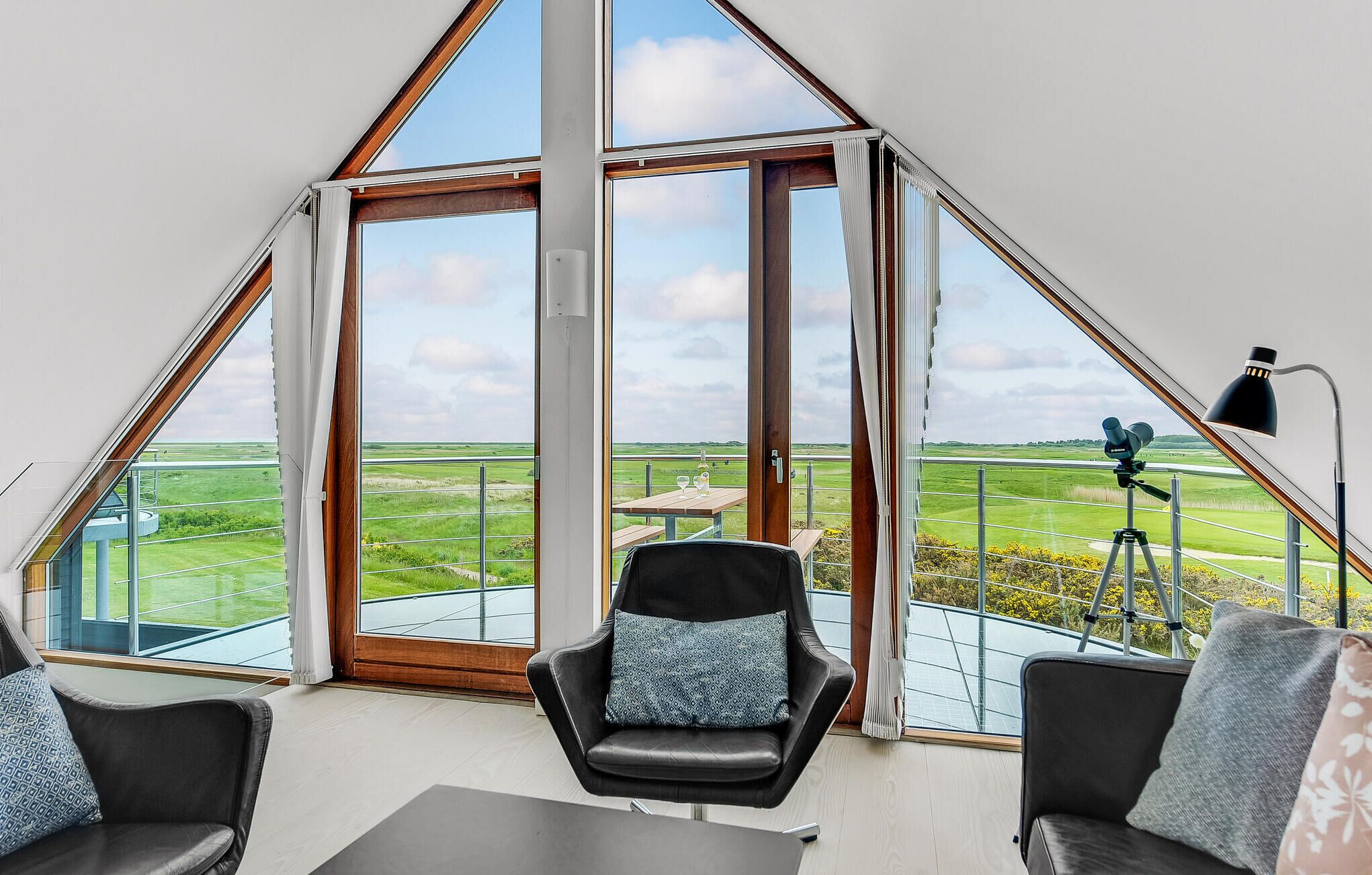 Ein Zimmer mit einem großen dreieckigen Fenster, einem Teleskop und zwei mit Kissen ausgestatteten Stühlen.