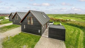 A modern house with a dark exterior, a sloped roof, and a paved driveway leading to a wooden door. - Amazing home in Rømø with sauna (Rømø)