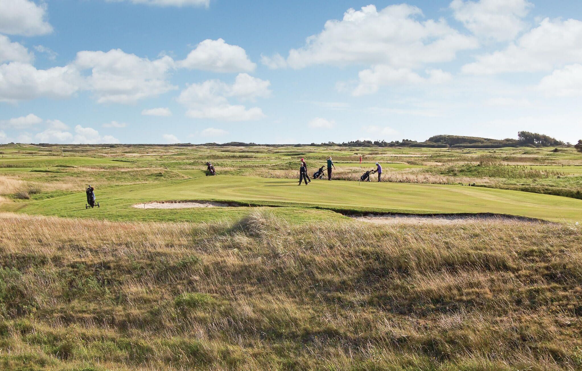 A golf course with a clear sky, rolling green hills, and a few golfers in the distance.