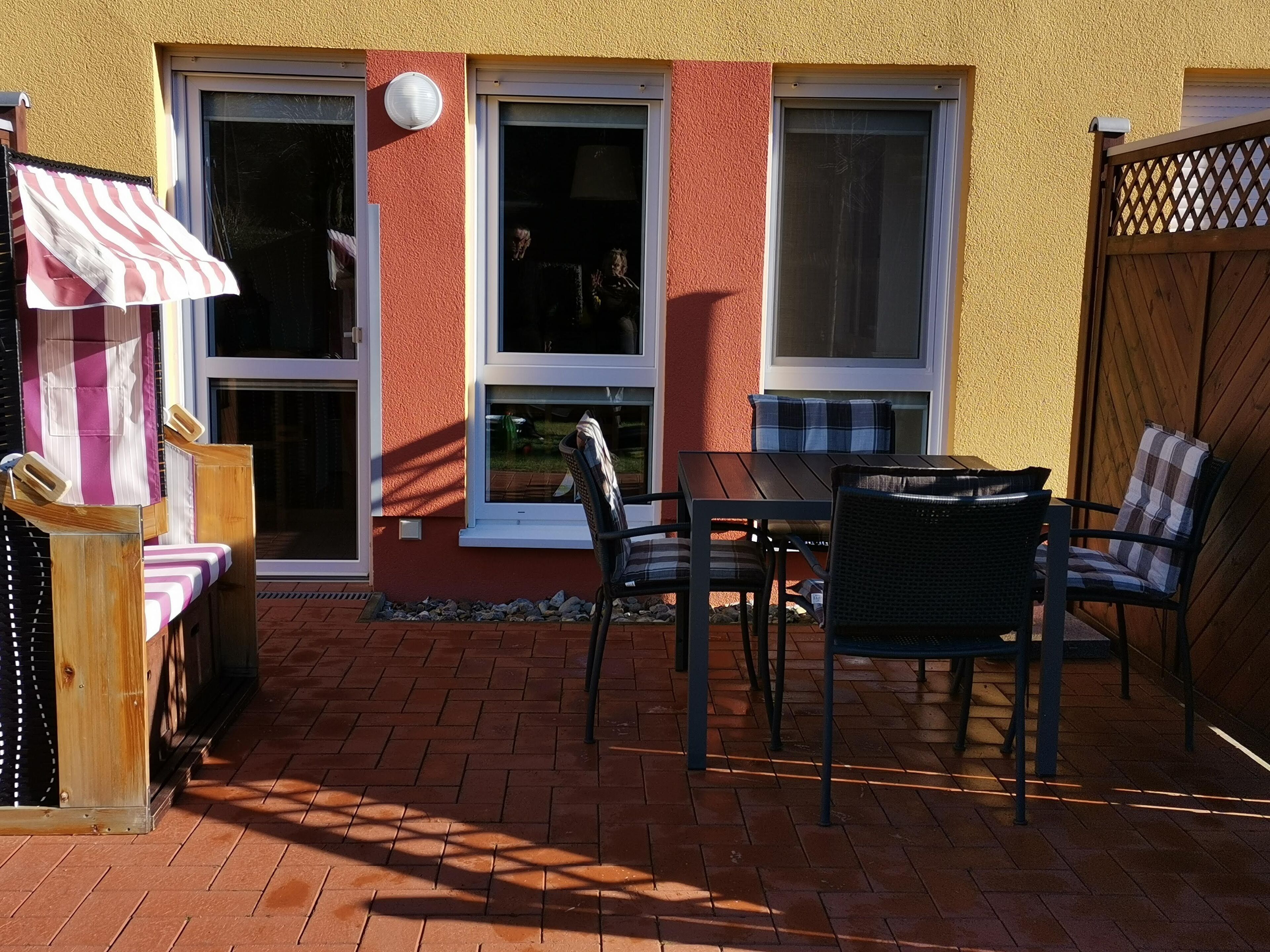 A patio with a table and chairs, a wooden fence, and a building with windows.