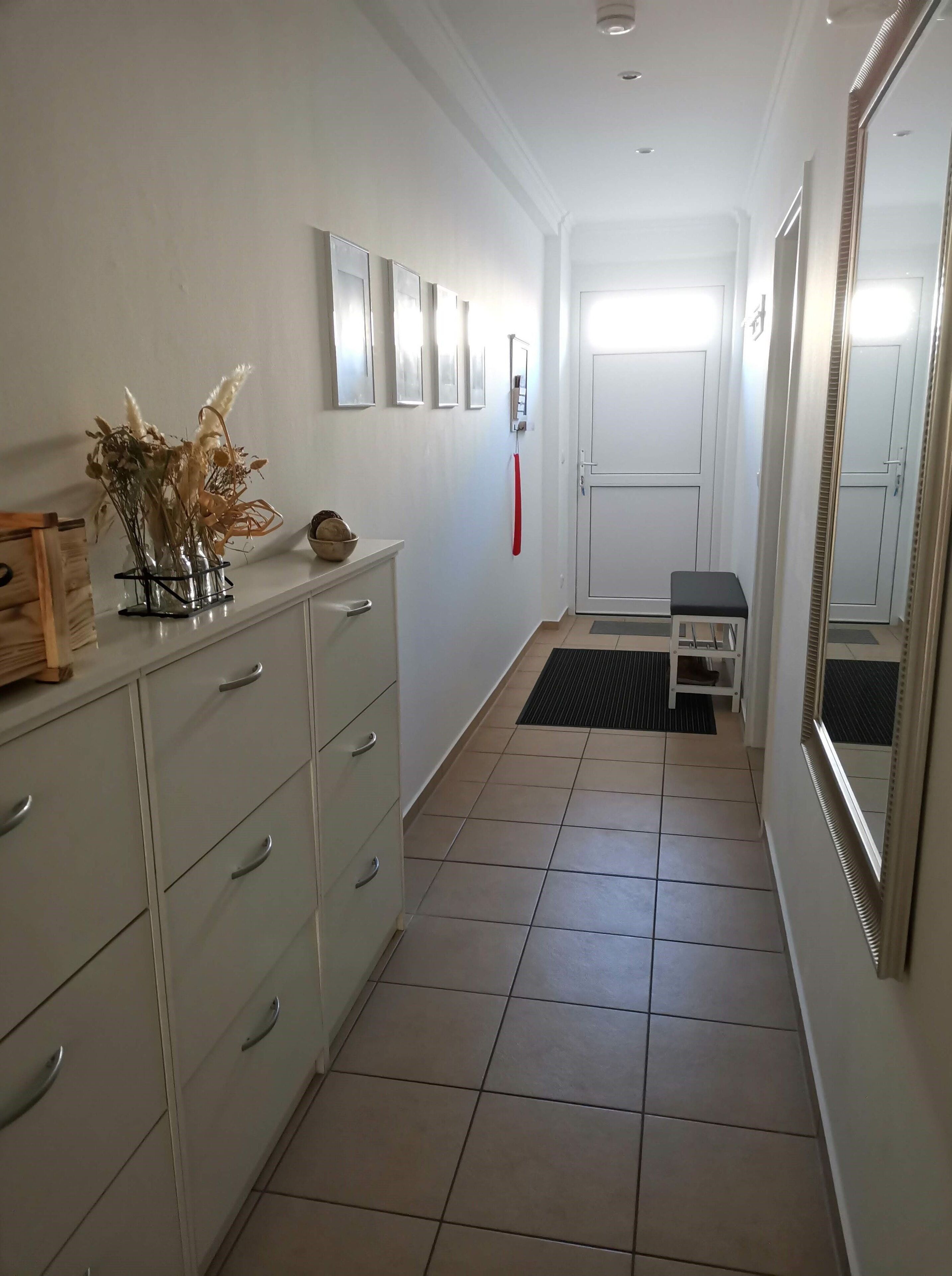 A hallway with a white dresser, a mirror, and a door.
