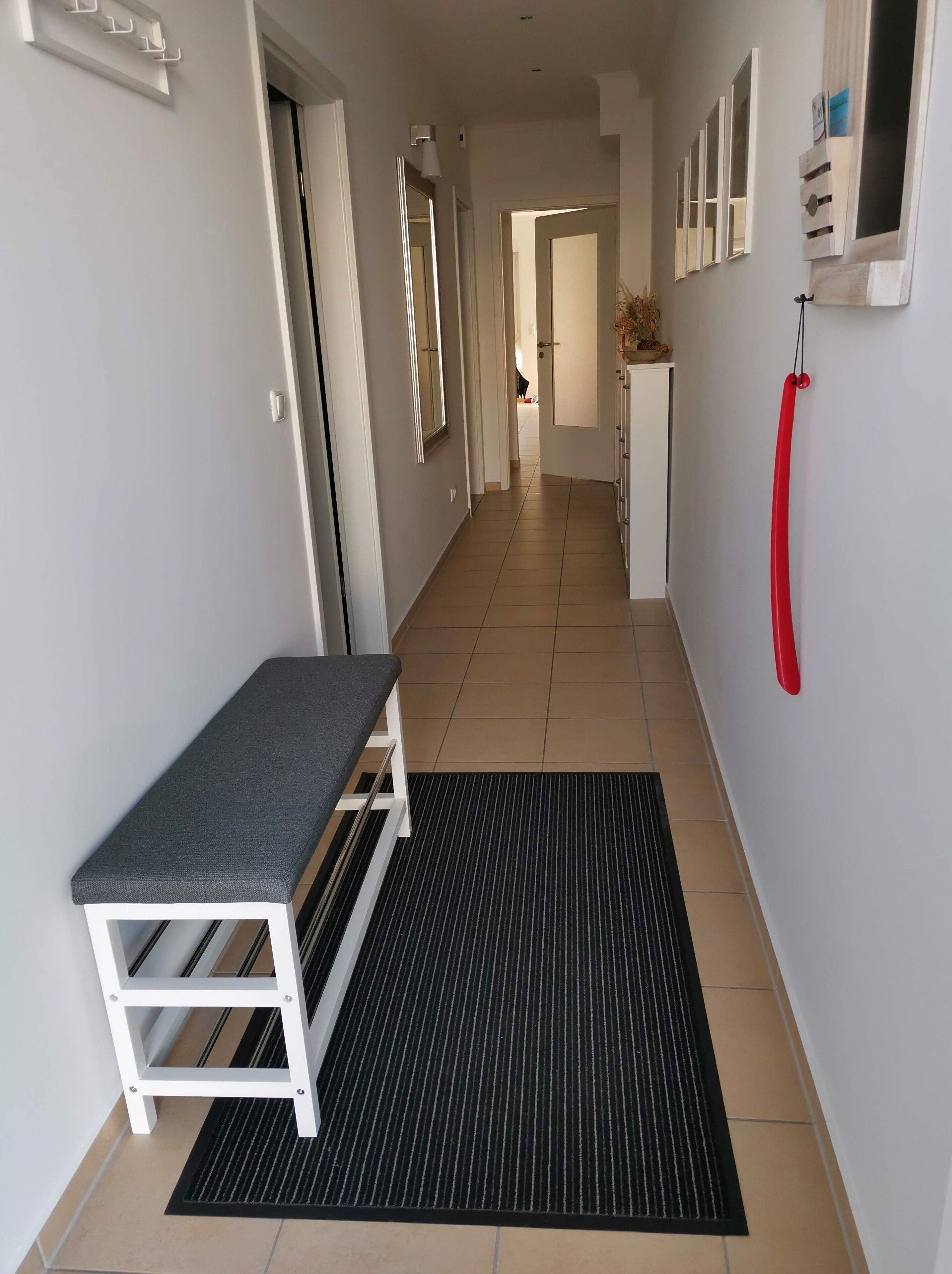 A hallway with a bench, a black mat, and a red object on the wall.
