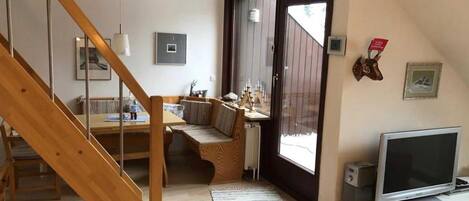 Uma sala de estar moderna com escada de madeira, área de jantar, televisão e uma grande janela.