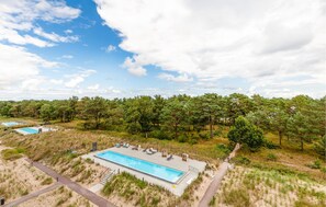 Ein Schwimmbecken mit Sonnendeck, umgeben von Dünen und Bäumen.
