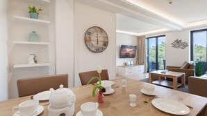 A dining area with a wooden table set for tea, a vintage clock, and a television in the background.