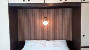 Una habitación de hotel con cama, lámpara de pared y un armario sobre la cama.