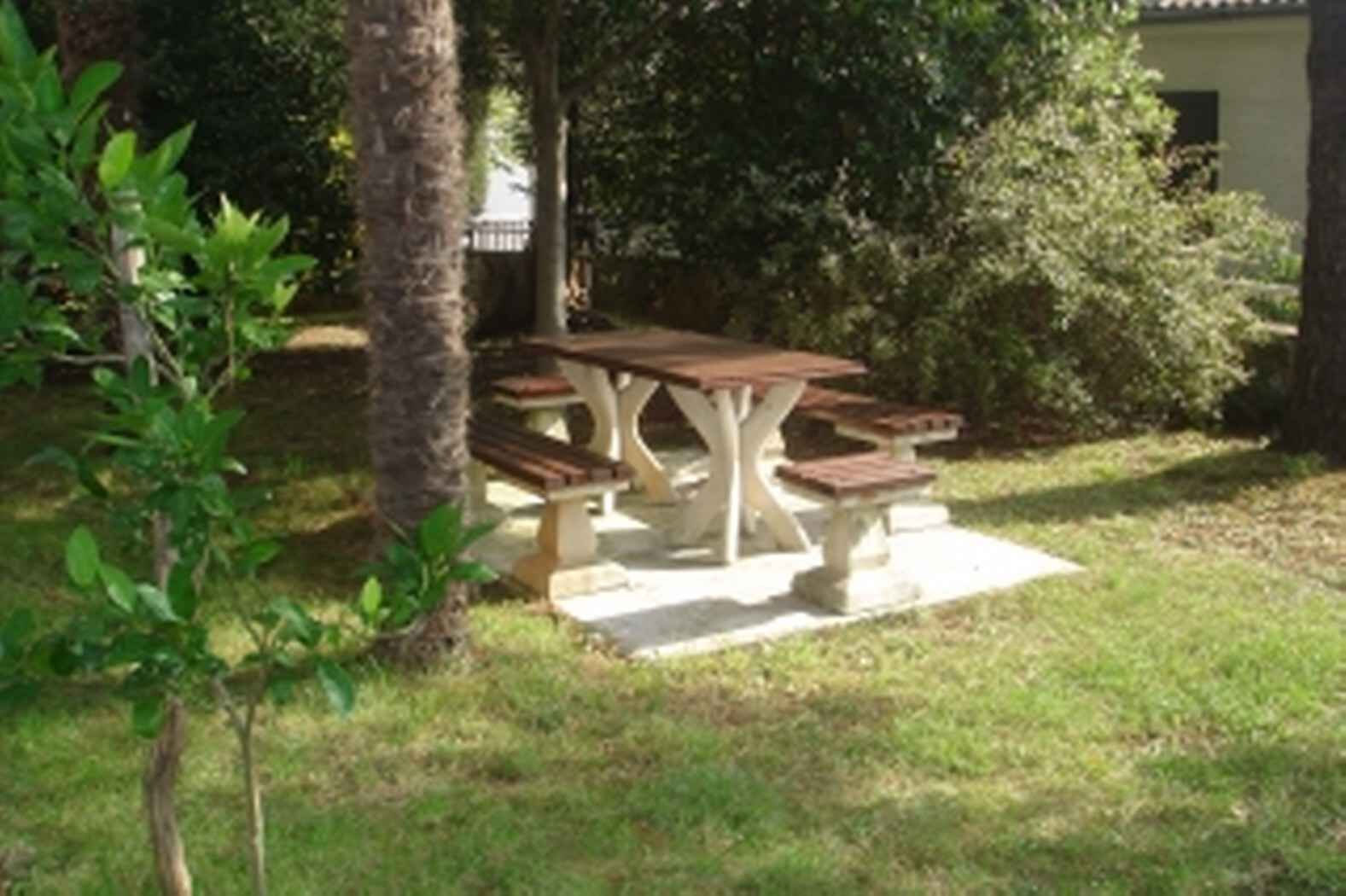 Een picknicktafel met banken in een grasveld, met bomen en een gebouw op de achtergrond.