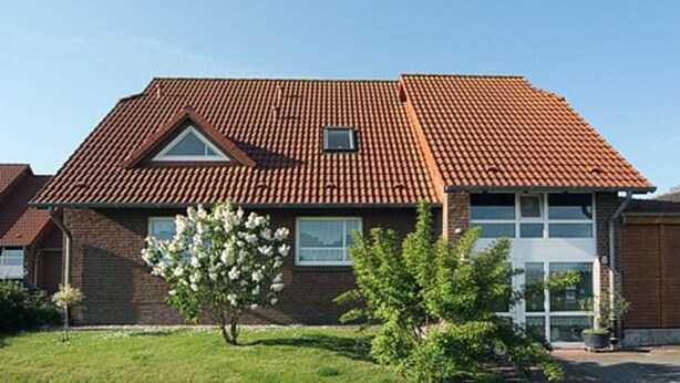 A two-story house with a red-tiled roof, a small window, and a garage door. - Apartment Achterloog (Werdum)