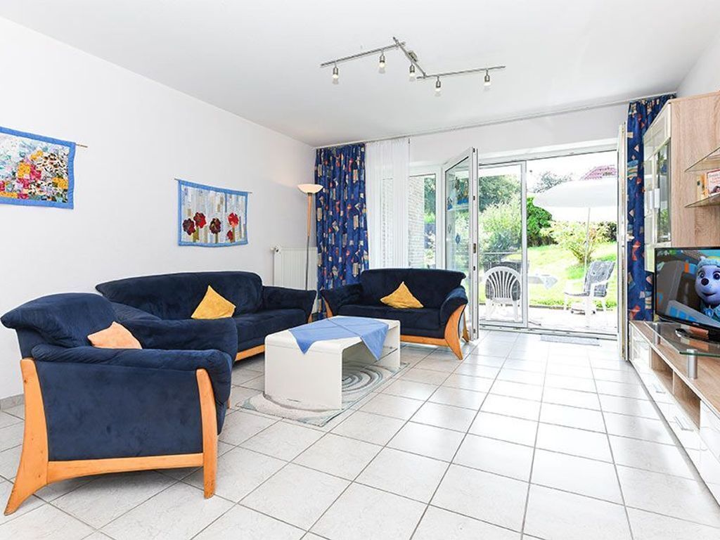 Een moderne woonkamer met twee donkerblauwe banken, een witte salontafel en een glazen deur naar een tuin.
