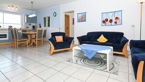 A living room with a sofa, a coffee table, and a dining area with chairs and a table. - Apartment Achterloog (Werdum)