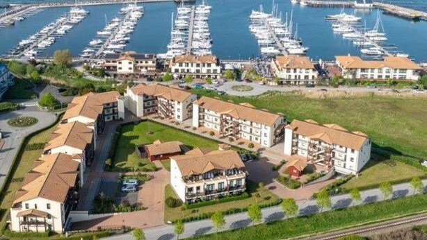 A coastal hotel with multiple buildings, a marina with boats, and a railway track nearby. - (259) 3-room apartment-Hafenstrasse-lake view - apartment complex vacation dreams (Kühlungsborn)