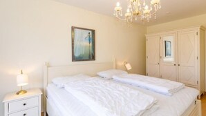 A bedroom with two beds, a nightstand with a lamp, a chandelier, and a wardrobe. - (259) 3-room apartment-Hafenstrasse-lake view - apartment complex vacation dreams (Kühlungsborn)