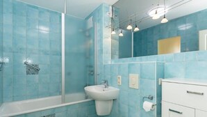 A bathroom with blue tiles, a white bathtub, a sink, and a toilet. - (259) 3-room apartment-Hafenstrasse-lake view - apartment complex vacation dreams (Kühlungsborn)