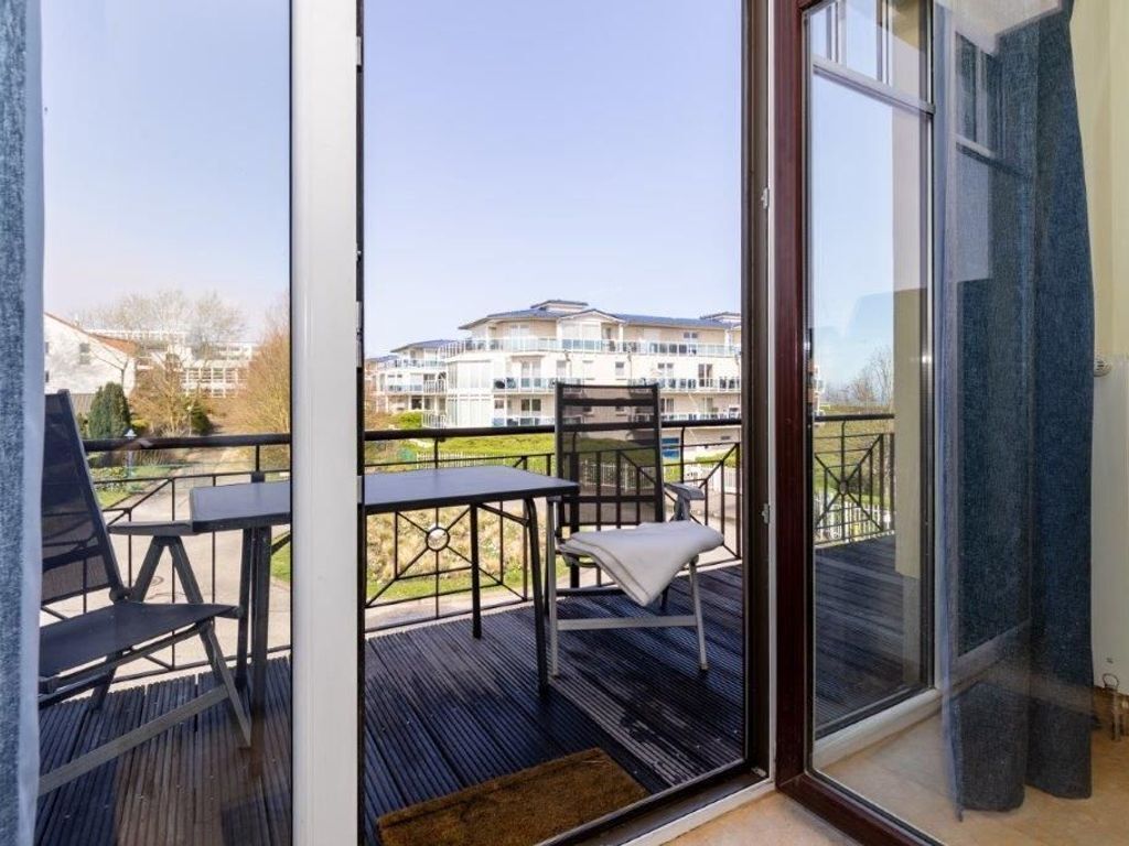 A balcony with a table and chairs, a view of a building in the background, and a glass door leading to the interior.