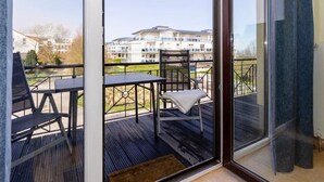 A balcony with a table and chairs, a view of a building in the background, and a glass door leading to the interior. - (259) 3-room apartment-Hafenstrasse-lake view - apartment complex vacation dreams (Kühlungsborn)