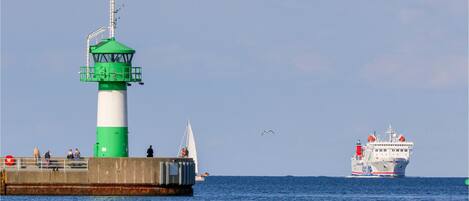 A lighthouse with a green and white structure, a pier with people, and a large ship in the background.