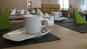 Een eetgedeelte met tafels gedekt voor het ontbijt, inclusief witte kopjes, schotels en een theepot.