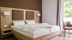 Een moderne slaapkamer met een houten hoofdbord, een groot bed met witte lakens, twee bedlampen, een nachtkastje en uitzicht op groen buiten.