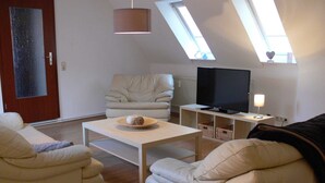 A modern living room with a sofa, a coffee table, a television, and a lamp. There are skylights on the ceiling. - Apartment Monima - Apartment (Bergen auf Rügen)