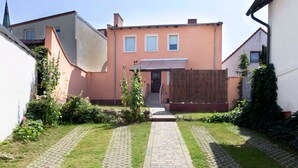 A residential property with a paved pathway leading to a wooden gate, surrounded by greenery and a pink building. - Apartment Monima - Apartment (Bergen auf Rügen)