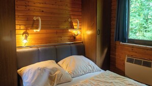 Una habitación de cabaña de madera con cama, cabecera, lámparas de noche y ventana con cortinas.