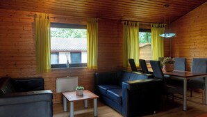 Interior acogedor de una cabaña con techo de madera, un sofá, una mesa de comedor con sillas y una pequeña mesa con una planta.