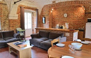 Un salon chaleureux avec un mur en briques, un canapé, une table basse et un coin repas comprenant une table et des chaises en bois.