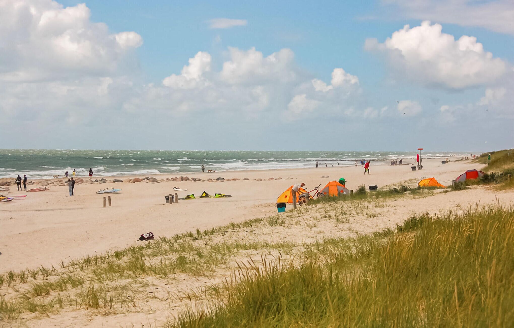 Una playa con tiendas de campaña, una bicicleta y gente caminando.
