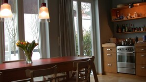 Una cocina con una mesa de madera, sillas, una estufa y un estante con utensilios de cocina.
