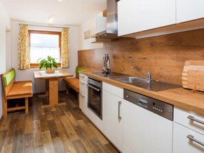 Una cocina funcional con encimera de madera, horno integrado, lavavajillas y ventana con cortinas.