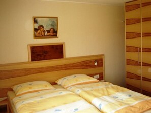 A double bed with a wooden headboard, a painting above it, and a wardrobe with a striped pattern.