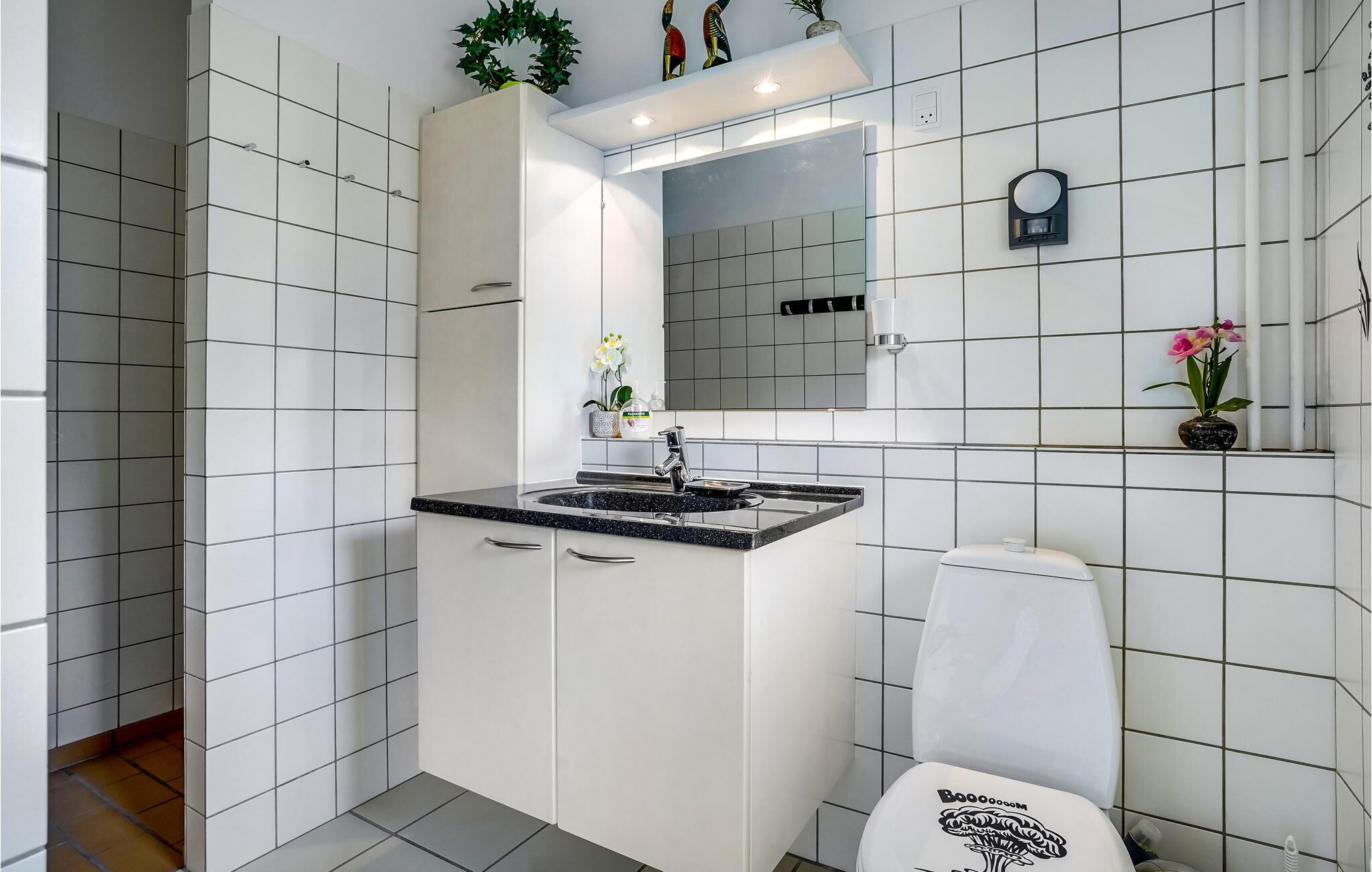 Een moderne badkamer met witte tegels, een zwart aanrecht wastafel, toilet en een spiegel boven de wastafel.
