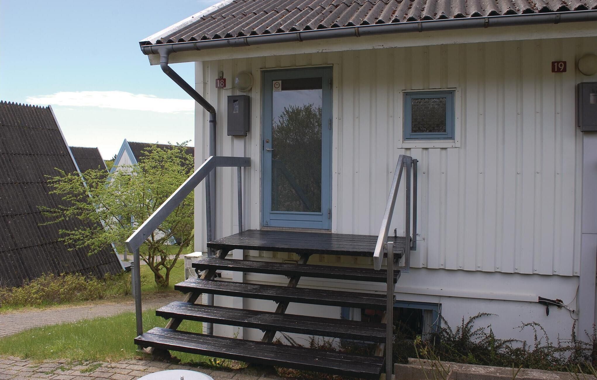 Ein kleines, eingeschossiges Gebäude mit einer blauen Tür und einer Treppe aus Holz, die zum Eingang führt.