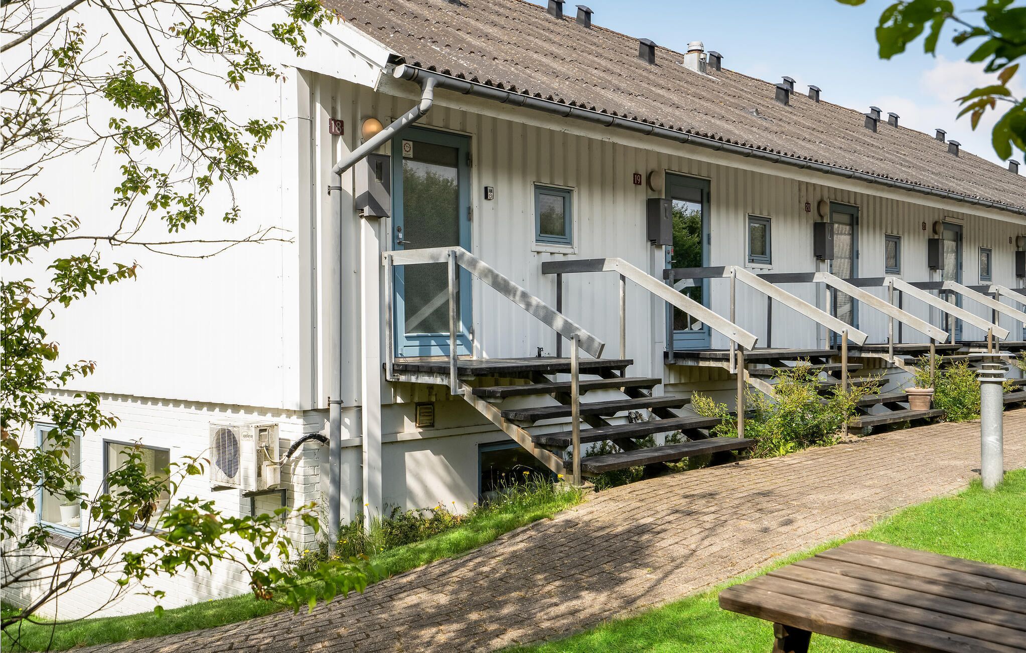 Un bâtiment doté de nombreuses fenêtres, d’un escalier et d’un espace pavé avec un banc.