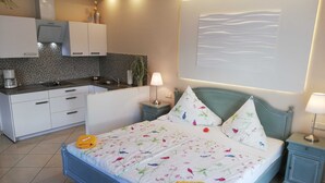 Ein modernes Schlafzimmer mit Bett, Nachttischen, einem kleinen Schreibtisch und einer Küchenzeile.