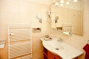 Casa de banho com lavatório branco, espelho, porta-toalhas e dispensador de toalhas.