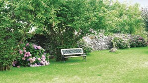 A bench in a garden with a stone wall and lush greenery.
